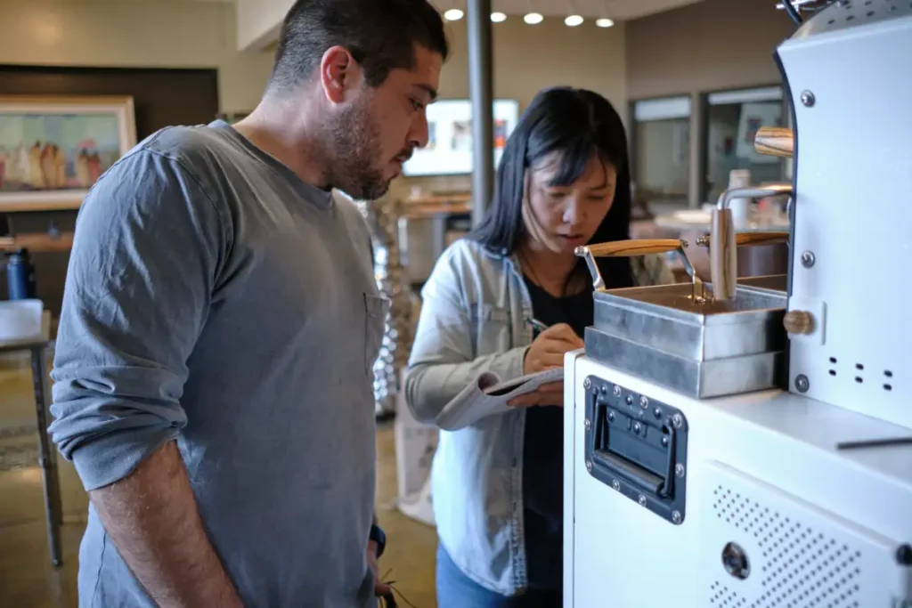 a man and woman standing next to a coffee roaster